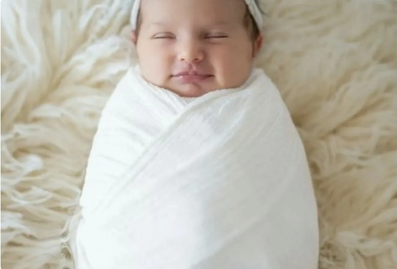 A newborn baby wrapped in a white blanket, sleeping.
